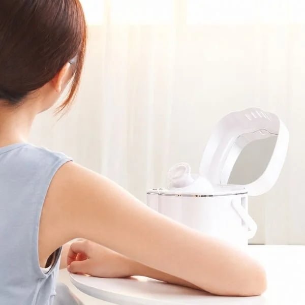 Woman seated beside the KD2332 facial steamer with flip-up mirror