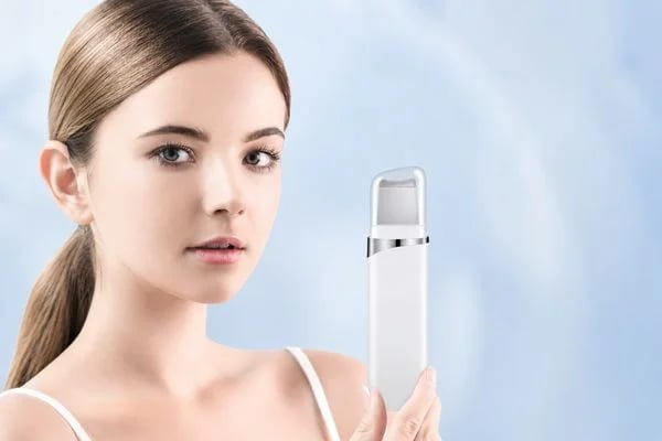 Woman holding the KD8023 ultrasonic facial skin scrubber against a light blue background